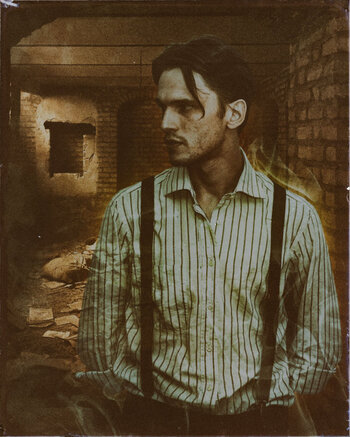 A man standing in front of a ruined room. He looks stern and serious, and whisps of smoke is hinted around him.